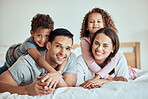 Portrait of happy family with little kids lying on the bed at home. Smiling couple bonding with their son and daughter in the morning at home. Adorable boy and girl lying on their mother and father