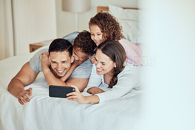 Buy stock photo Young happy mixed race family smiling for a selfie lying on a bed together at home. Hispanic woman smiling taking a photo with her children and husband with her cellphone relaxing in a bedroom