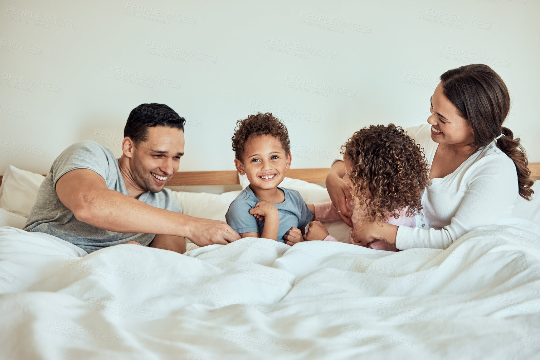 Buy stock photo Mixed race Family lying in bed smiling and playing. Latino parents having fun with their little cute kids