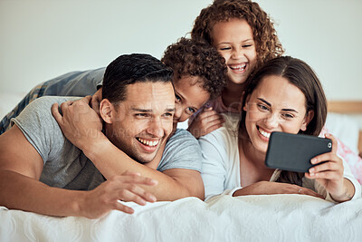Buy stock photo Family taking a selfie with a cellphone in bed. Happy hispanic family taking photos in bed on a smartphone. Parents making memories with their children. Excited children taking pictures 
