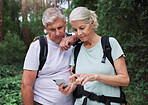 A mature couple using a cellphone while out on a hike together. Senior caucasian husband and wife using a wireless device in a forest