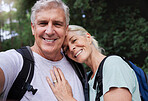 Portrait of a senior caucasian couple smiling and taking a selfie in a forest during a hike in the outdoors. Man and wife showing affection and holding each other during a break in nature