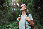 Portrait of a woman wearing a backpack hiking through a forest in nature alone. Female walking on a trail in the outdoors and smiling while enjoying the view