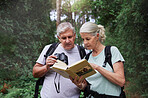 Senior caucasian couple using binoculars and a book while doing bird watching in a forest during a hike. Mature husband and wife exploring in a forest