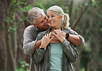 A senior caucasian couple smiling and looking happy in a forest during a hike in the outdoors. Man and wife showing affection and holding each other during a break in nature