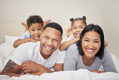 Buy stock photo Portrait of a cheerful family with two children lying together on bed. Little boy and girl lying on their parents laughing and having fun. Hispanic siblings enjoying free time with their mother and father