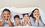 Portrait of happy family with two children lying under duvet smiling and looking at camera. Little girl and boy lying in bed with their parents bonding and having fun