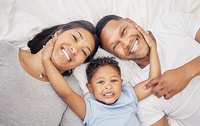 Buy stock photo Adorable little boy lying between his mother and father from above. Loving parents bonding with their son lying on a bed at home