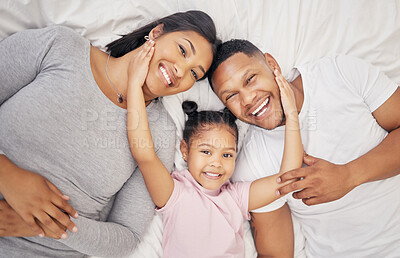 Adorable little girl pulling her parents close while lying between her mother and father from above. Loving parents bonding with their daughter lying on a bed and spending free time together on the weekend
