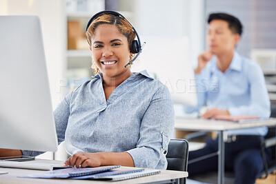 Portrait of one happy young mixed race female call centre telemarketing agent talking on a headset while working on a computer in an office. Confident and friendly african american businesswoman consultant operating helpdesk for customer service support