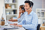 Happy young asian male call centre telemarketing agent talking on a headset while working on a computer in an office. Confident and friendly businessman consultant operating a helpdesk for customer service support