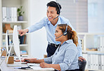 Young asian call centre telemarketing agent training new african american assistant on a computer in an office. Team leader troubleshooting solution with intern for customer service and sales support. Colleagues operating helpdesk together