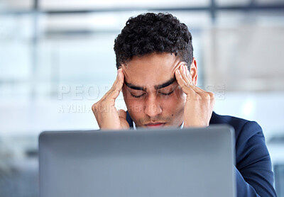 One exhausted mixed race businessman rubbing forehead with headache and computer vision eye strain while working on laptop in an office. Young entrepreneur feeling overworked, tired and anxious about deadlines. Mentally frustrated with burnout and stress