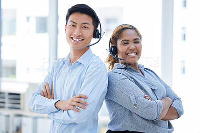Portrait of two happy smiling diverse call centre telemarketing agents standing back to back with arms crossed while wearing headset in an office. Confident and friendly african american and asian assistants providing customer service support