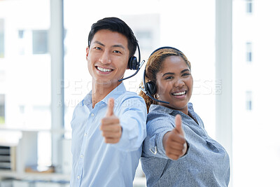 Portrait of two happy smiling diverse call centre telemarketing agents standing back to back and gesturing thumbs up for success while wearing headset in an office. Confident and friendly assistants giving good customer service