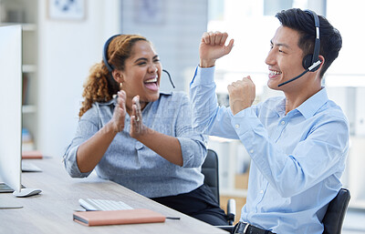 Two happy young call centre telemarketing agents clapping and cheering with joy while working together in an office. Excited african american and asian assistants celebrating successful sales and reaching targets to win