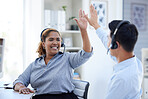 Two happy young call centre telemarketing agents giving each other a high five while cheering with joy in an office. Excited african american assistant celebrating with colleague on successful sales and reaching targets to win