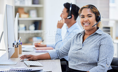 Young happy mixed race female call center agent working on a computer while answering calls in an office at work. Hispanic female customer service agent smiling wearing a headset on a call