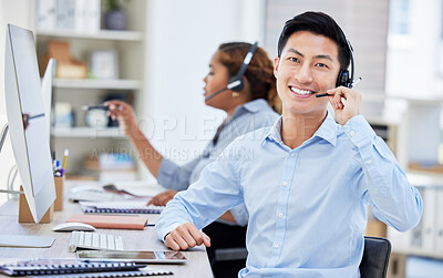 Portrait of asian call centre agent talking on headset while working on computer in office. Confident and smiling businessman consulting and operating a helpdesk for customer sales and service support