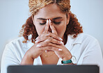 Closeup of a mixed race businesswoman suffering from a headache working on a laptop alone at work. Hispanic woman stressed while working. Female boss looking anxious. Businessperson looking tired

