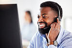 One happy young african american male call centre telemarketing agent talking on a headset while working on a computer in an office. Confident and friendly businessman consultant operating a helpdesk for customer service support