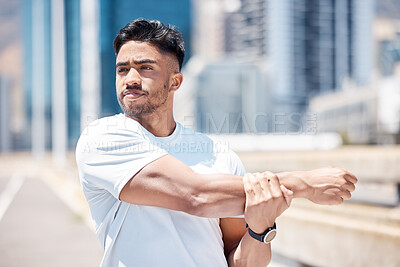 Fit young mixed race man stretching his arms before his run outdoors on a city road. Handsome male athlete warming up and getting ready for a cardio workout