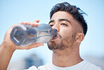 Young male athlete taking a break and drinking water from a bottle while out for a run and exercising outdoors during the day