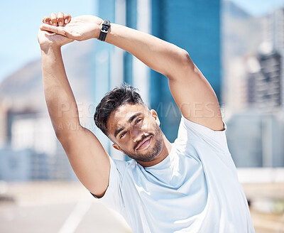 Fit young mixed race man stretching his arms above his head before his run outdoors on a city road. Handsome male athlete warming up and getting ready for a cardio workout