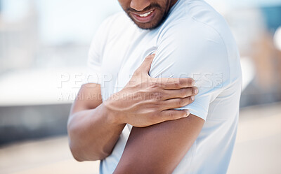 Close up view of a man holding his arm and suffering from shoulder pain during his outdoor workout. Mixed race male athlete feeling discomfort from a sports injury while exercising in the city
