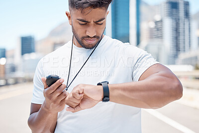 Young mixed race male athlete checking digital chronometer and smart watch to track time during a workout. Sportsman monitoring his performance or progress during a run in the city