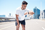 Athletic young mixed race man looking at his watch while exercising outdoors. Handsome mixed race male looking serious while checking the time on his smartwatch after a run. Tracking progress while working out