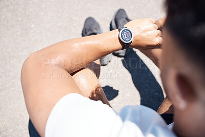 Sweaty athletic man sitting and looking at his digital watch while resting after a workout outdoors. Over the shoulder view of fit male checking the time on his smartwatch after a run. Tracking progress while working out