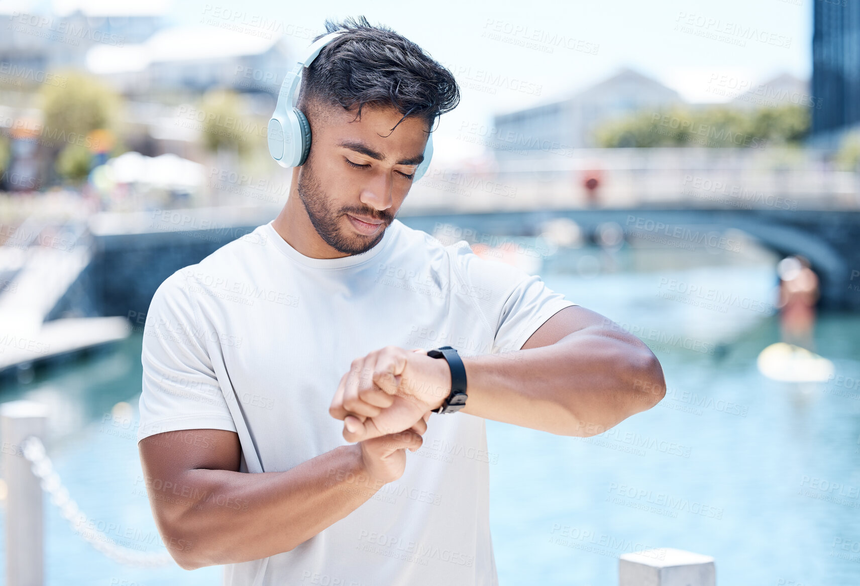 Buy stock photo Fitness, music and man in city with smart watch for running, exercise and tracking workout. Headphones, sports and male person check wristband for marathon training, wellness and performance time