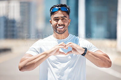 Happy young male athlete making heart shape with hands while standing on city road. Fit sportsman out for a run outdoors because cardio exercise is good for the heart health