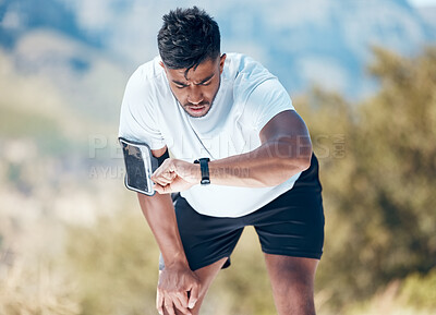Athletic young mixed race man looking at his watch while exercising outdoors. Handsome indian looking serious while checking the time on his smartwatch during a workout. Tracking progress while working out