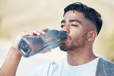 Closeup of a handsome mixed race young man drinking water with a bottle, standing alone and taking a break during his outdoor workout