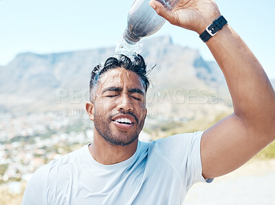 Closeup of a handsome young man standing alone and pouring water on his face after a run outdoors. Fit indian male getting hot and cooling down with some water after a exercise
