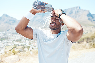 Closeup of a handsome young man standing alone and pouring water on his face after a run outdoors. Fit indian male getting hot and cooling down with some water after a exercise