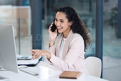 Young happy mixed race businesswoman on a call using her phone and desktop computer pointing her finger in an office at work. One hispanic businesswoman smiling while sitting at a desk and talking on her cellphone at work