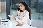 Young happy mixed race businesswoman on a call using her phone and desktop computer making a hand gesture in an office at work. One hispanic businesswoman smiling while sitting at a desk and talking on her cellphone at work
