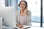 Young happy mixed race businesswoman wearing headphones listening to music while writing in a notebook alone in an office. One hispanic businessperson smiling listening to music and writing ideas sitting at an office desk