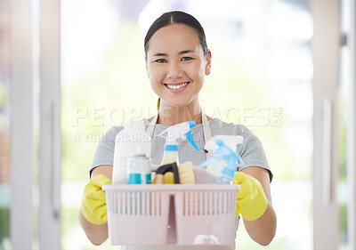 One cheerful mixed race woman holding cleaning supplies while cleaning her apartment. An Asian domestic cleaner wearing latex cleaning gloves with a collection of cleaning products