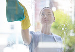 A beautiful young mixed race domestic worker using a cloth on a window. One Asian woman enjoying doing chores in her apartment