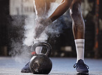 Closeup of unknown african american athlete using powder and chalk on hands before lifting kettlebell in gym. Strong, fit, active black man getting ready to workout. Weightlifting in exercise routine