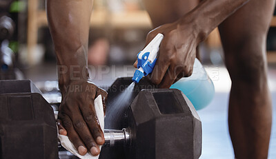 Closeup of unknown african american athlete using spray bottle to sanitise dumbbell weights in gym. Active black man cleaning equipment in hygiene routine to protect and prevent covid through exercise