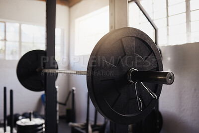 Heavy barbell weights and bar arranged in empty gym with nobody during day. Metal weightlifting equipment organised in a health club and sports centre with no one inside. Healthy exercise routine
