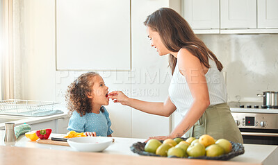 Buy stock photo Mother feeding child vegetables while cooking together in the kitchen. Mom and daughter spending time together at home. Vegetables are good for you