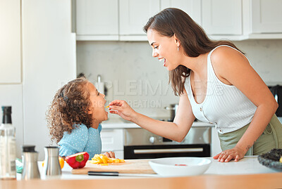 Mother feeding child vegetables while cooking together in the kitchen. Mom telling daughter to open wide and eat her vegetables