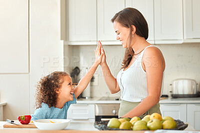 Cheerful mother and daughter giving each other a high-five at home. Mom and little girl cooking together in the kitchen. Little girl chopping vegetables under adult supervision