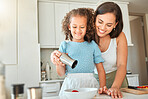 Happy mother teaching little daughter to cook in kitchen at home. Little girl adding seasoning to a bowl while making a salad with mom